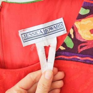 May include: Red sleeveless dress with a colorful floral print and a white tag that says "Jessica Howard".