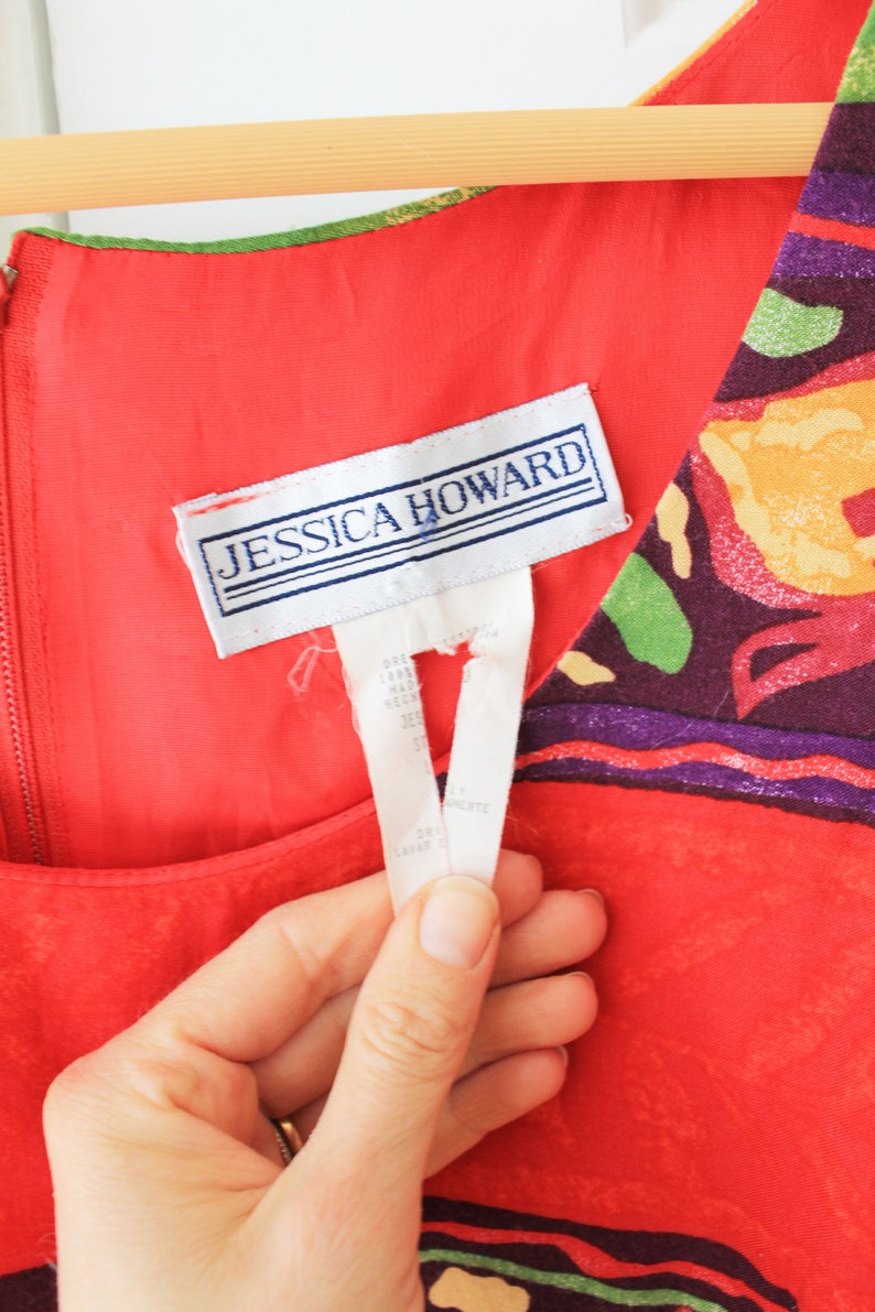 May include: Red sleeveless dress with a colorful floral print and a white tag that says "Jessica Howard".