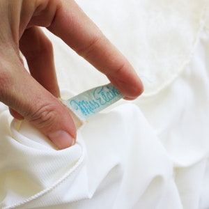 May include: A white fabric label with blue text that reads "Miss Elaine".