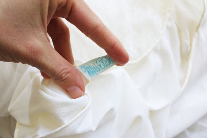 May include: A white fabric label with blue text that reads "Miss Elaine".