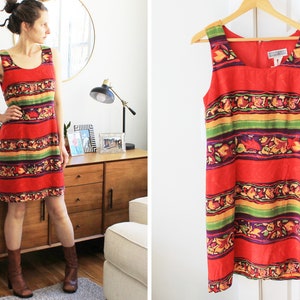 May include: A sleeveless red dress with a colorful striped and floral pattern. The dress has a scoop neck and a straight silhouette.