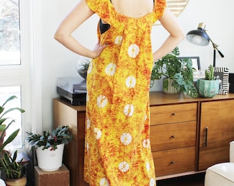 May include: A yellow and orange maxi dress with a white floral pattern. The dress has a scoop neck and ruffled straps.