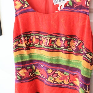 May include: A red sleeveless dress with a colorful floral and geometric pattern. The dress has a scoop neck and a zipper closure in the back. The dress has a label that reads "Jessica Howard!"