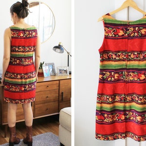 May include: A sleeveless red dress with a colorful striped pattern featuring green, yellow, purple, and orange accents. The dress has a scoop neck and a straight silhouette.