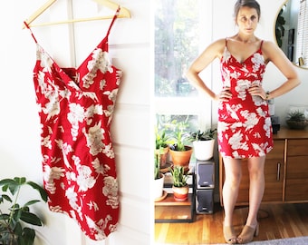 May include: A red and white floral print mini dress with thin straps. The dress has a V-neckline and a wrap-style bodice.