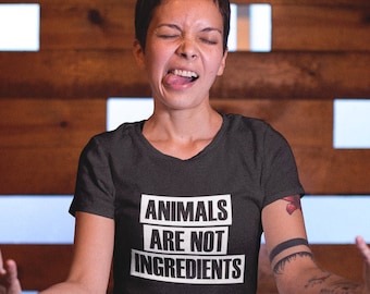 May include: A person wearing a black t-shirt with the text "ANIMALS ARE NOT INGREDIENTS" in white letters. The person is sitting with their legs crossed and their hands raised in the air.