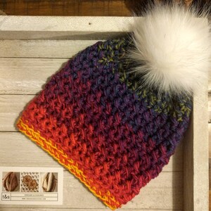 May include: A colourful crocheted beanie with a white faux fur pom pom. The beanie is made with a gradient yarn in shades of red, orange, yellow, purple, and blue. The beanie has a yellow crocheted border.