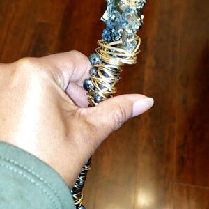 May include: A gold wire-wrapped wand with a large, rough, pyrite crystal at the top. The wand is decorated with black beads.
