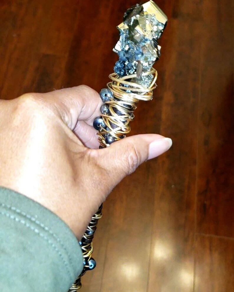 May include: A gold wire-wrapped wand with a large, rough, pyrite crystal at the top. The wand is decorated with black beads.