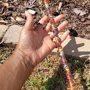 May include: A copper wire wrapped wand with amethyst crystals and colorful beads. The wand is held in a hand.