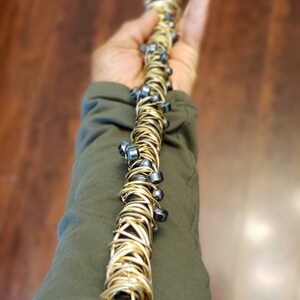 May include: A gold wire wrapped wand with black beads. The wand is held in a hand.