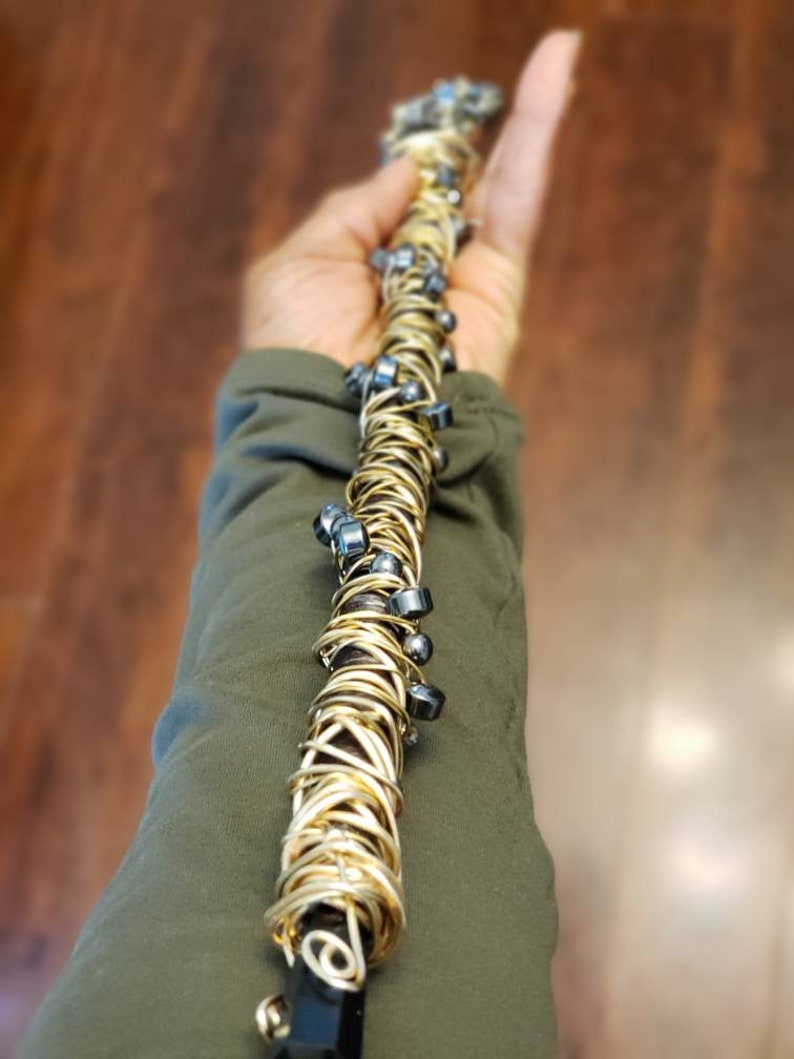May include: A gold wire wrapped wand with black beads. The wand is held in a hand.