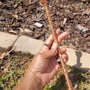 May include: A copper wire wrapped wand with a light blue crystal at the top. The wand is held in a hand.