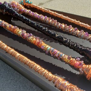 May include: Five copper wire wrapped wands with amethyst and other colorful beads. The wands are displayed on a black surface.