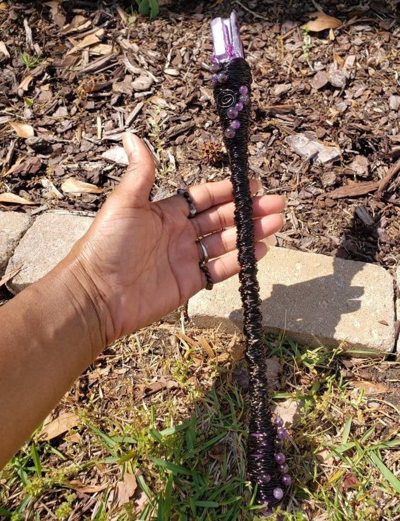 May include: A black wire-wrapped wand with purple amethyst crystals and a clear crystal point at the top.