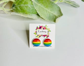 Op de afbeelding: Een paar regenboog-pride-vlag oorbellen op een witte kaart met de tekst "Creations by Chelsea" en een website-adres.