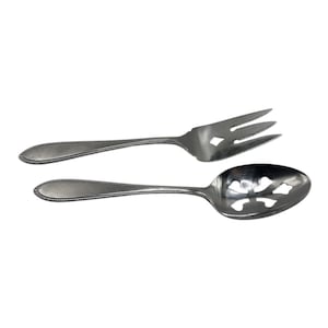Puede incluir: Un juego de tenedor y cuchara de servir plateados. El tenedor tiene tres púas y un recorte decorativo en forma de diamante. La cuchara tiene un cuenco ranurado con un diseño floral. Ambas piezas tienen un borde con cuentas.