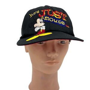 May include: Black baseball cap with a red brim. The front of the cap features an embroidered image of Mickey Mouse with the text "he's just a mouse".