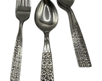 May include: A set of silver-colored flatware, including a fork and spoons, against a white background. The handles are decorated with a floral pattern. The spoons have a classic oval bowl shape.