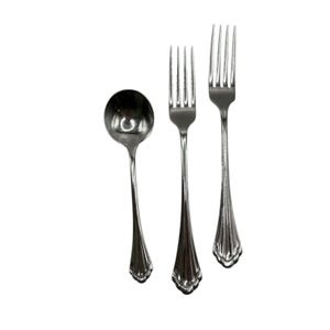 May include: A set of three silver-colored utensils: a soup spoon and two forks. The spoon has a rounded bowl. The forks have four tines and decorative handles. The silverware is arranged on a white background.