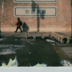 May include: A blurry image of a person walking past a brick wall with two signs. The top sign says "you are beautiful" and the bottom sign says "你很美丽" in Chinese characters.