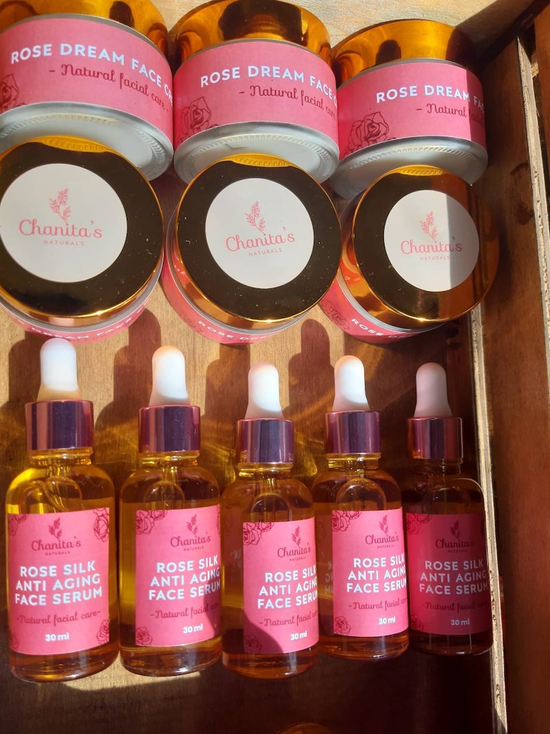 Puede incluir: Seis botellas de suero facial antienvejecimiento de seda de rosa en botellas de vidrio transparente con tapas y etiquetas doradas. Las botellas est&aacute;n dispuestas en una fila sobre una superficie de madera. Cada botella contiene 30 ml de suero. Las etiquetas muestran el nombre de la marca "Chanita's Naturals" y el nombre del producto "Suero facial antienvejecimiento de seda de rosa".
