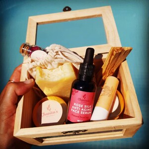Puede incluir: Caja de madera llena de productos de belleza naturales, incluyendo una botella de suero facial antiedad de seda de rosa, una barra de jab&oacute;n, un peque&ntilde;o tarro de crema y un palo de madera. La caja est&aacute; abierta y los productos son visibles.