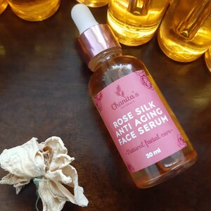 Puede incluir: Una botella de vidrio de suero facial antienvejecimiento de seda de rosa con una etiqueta rosa y un gotero. La etiqueta dice "Chanita's Naturals Rose Silk Anti-Aging Face Serum - Natural facial care - 30 ml".