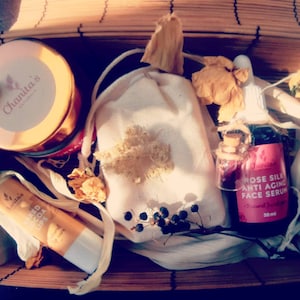 Puede incluir: Una caja de regalo llena de productos de belleza naturales. La caja contiene un tarro de crema facial, una peque&ntilde;a bolsa de flores secas, un b&aacute;lsamo labial y una botella de suero facial antiedad de seda de rosa. Todos los productos est&aacute;n etiquetados con el nombre de la marca "Chanta's Naturals".