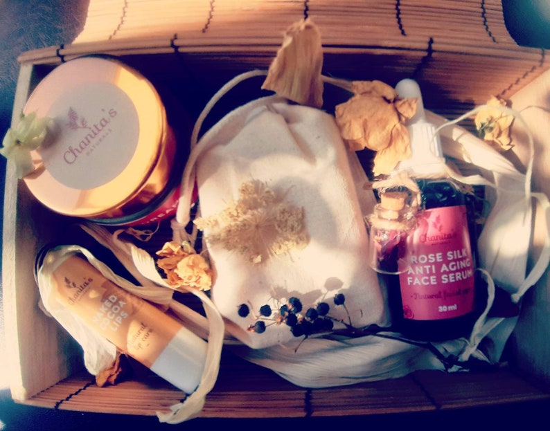 Puede incluir: Una caja de regalo llena de productos de belleza naturales. La caja contiene un tarro de crema facial, una peque&ntilde;a bolsa de flores secas, un b&aacute;lsamo labial y una botella de suero facial antiedad de seda de rosa. Todos los productos est&aacute;n etiquetados con el nombre de la marca "Chanta's Naturals".