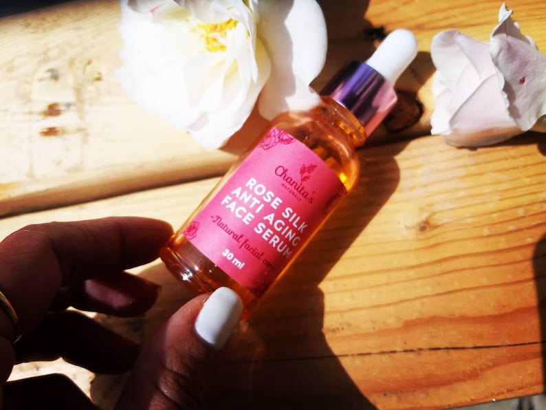 May include: A 30 ml bottle of rose silk anti-aging face serum by Chanita's Naturals. The bottle is clear glass with a pink / white top and a pink label with white text.
