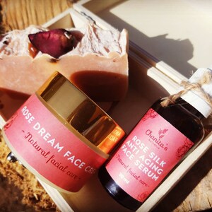 Puede incluir: Una caja de madera llena de un set de cuidado de la piel con aroma a rosa. El set incluye una barra de jab&oacute;n, un tarro de crema facial etiquetado como "ROSE DREAM FACE CREAM - Natural facial care", y una botella de suero facial etiquetada como "ROSE SILK ANTI AGING FACE SERUM - Natural facial care - 30 ml".