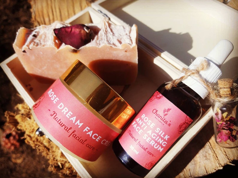 Puede incluir: Una caja de madera llena de un set de cuidado de la piel con aroma a rosa. El set incluye una barra de jab&oacute;n, un tarro de crema facial etiquetado como "ROSE DREAM FACE CREAM - Natural facial care", y una botella de suero facial etiquetada como "ROSE SILK ANTI AGING FACE SERUM - Natural facial care - 30 ml".