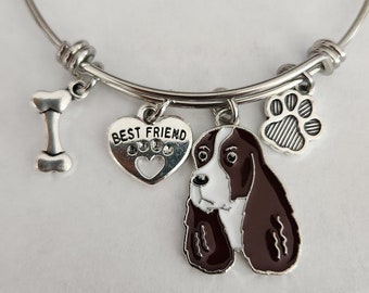 May include: Silver-toned bangle bracelet with multiple charms. Charms include a dog bone, a heart with the words "BEST FRIEND" and paw prints, a dog paw print, and a brown and white dog pendant.