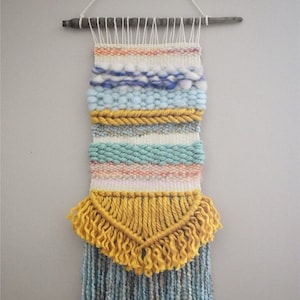 May include: A woven wall hanging with a yellow, blue, and white color scheme. The hanging has a fringe of yellow yarn at the bottom.