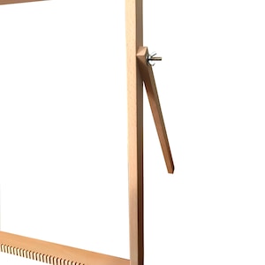 May include: A wooden loom with a natural finish. The loom has a rectangular frame with a tensioning system on one side. The loom is designed for weaving small projects.