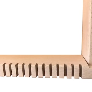 May include: Close-up of the bottom edge of a wooden frame with a series of evenly spaced slots cut into the wood.