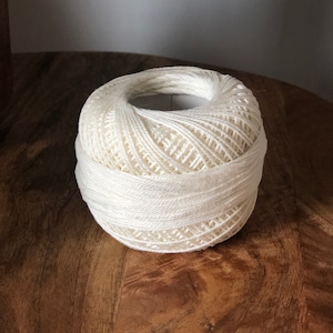 May include: A ball of white yarn on a wooden surface.