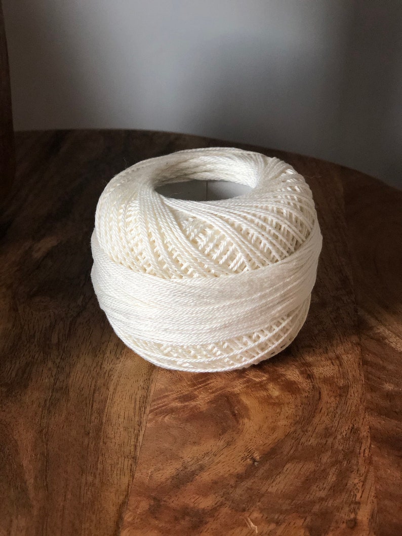 May include: A ball of white yarn on a wooden surface.