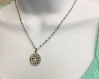 May include: A silver chain necklace with a circular pendant featuring a geometric design. The pendant is made of metal and has a detailed pattern of triangles and circles.