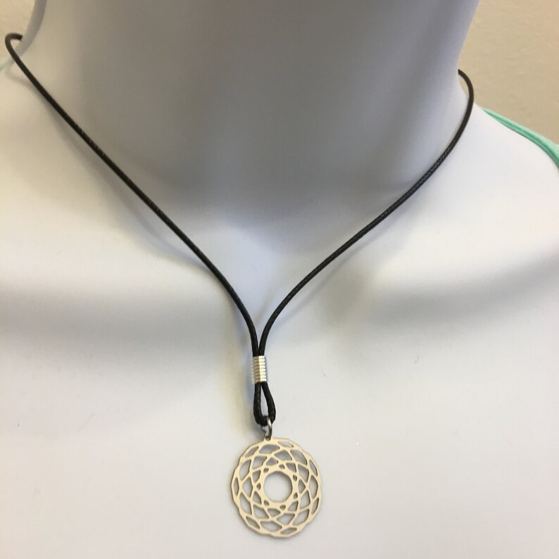 May include: A silver pendant necklace with a geometric design hangs from a black leather cord.