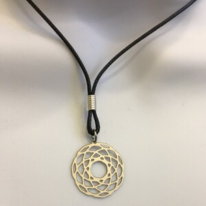 May include: A silver pendant necklace with a geometric design hangs from a black cord. The pendant is a circle with a intricate pattern of lines and curves.
