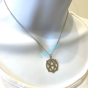 Op de afbeelding: Een zilveren ketting met een zilveren hanger met een gestileerde letter "A" in een cirkel. De hanger heeft een geometrisch ontwerp.