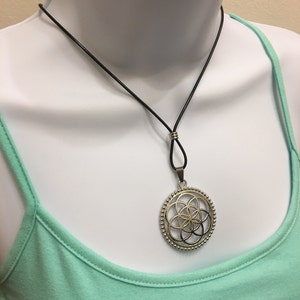 May include: A silver pendant necklace with a circular design featuring a geometric pattern. The necklace is on a black leather cord.