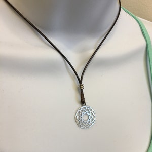 May include: A silver pendant necklace with a circular geometric design hangs from a brown leather cord.