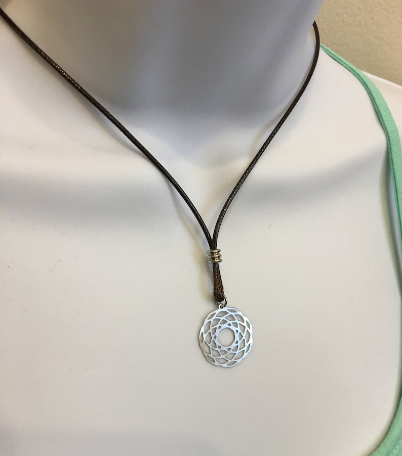 May include: A silver pendant necklace with a circular geometric design hangs from a brown leather cord.