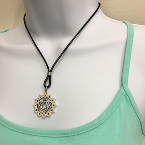 May include: A silver pendant necklace with a chakra symbol on a black leather cord. The pendant is a star-shaped design with a symbol in the centre.