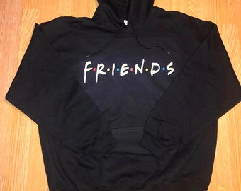May include: Black hooded sweatshirt with the word "FRIENDS" printed across the chest in white, red, blue, and yellow. The sweatshirt has a front pocket and a drawstring hood. The design is a reference to the popular TV show.