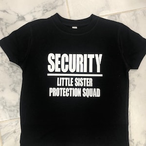 May include: Black t-shirt with white text that reads "SECURITY LITTLE SISTER PROTECTION SQUAD".