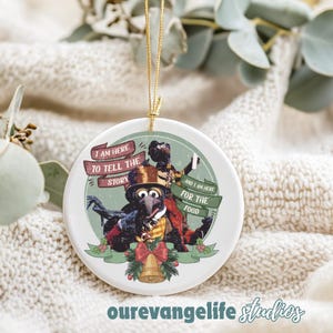 May include: A round white Christmas ornament with a cartoon image of Gonzo and another Muppet character. The ornament has the text "I AM HERE TO TELL THE STORY" and "AND I AM HERE FOR THE FOOD". A gold string is attached.